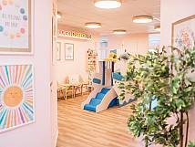 Heller Raum mit Spielschiff, bunten Postern, Pflanzen und Sitzmöglichkeiten für Kinder